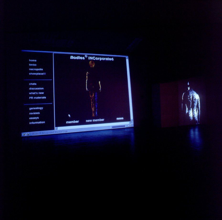 Installation in a dark room showing two screens set up next to each other displaying a webpage interface with a menu column and a human body in between white text on the left and the back of a body from the head down to butt on the right.